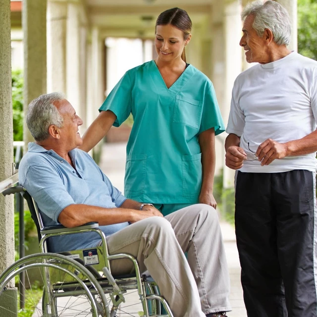A senior man in a wheelchair talks with a senior man and a senior living staff member