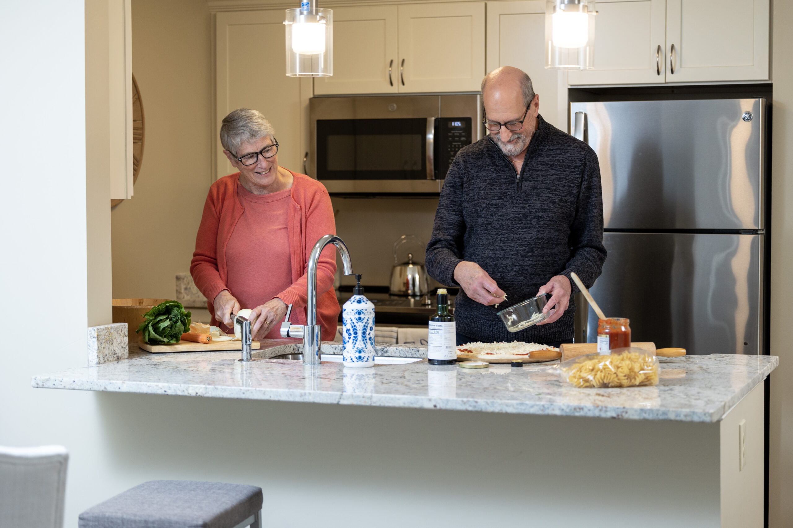 Residents Ken and Mary Lu Love prepare a meal together in a bright, modern apartment kitchen, chopping vegetables and assembling ingredients side by side.