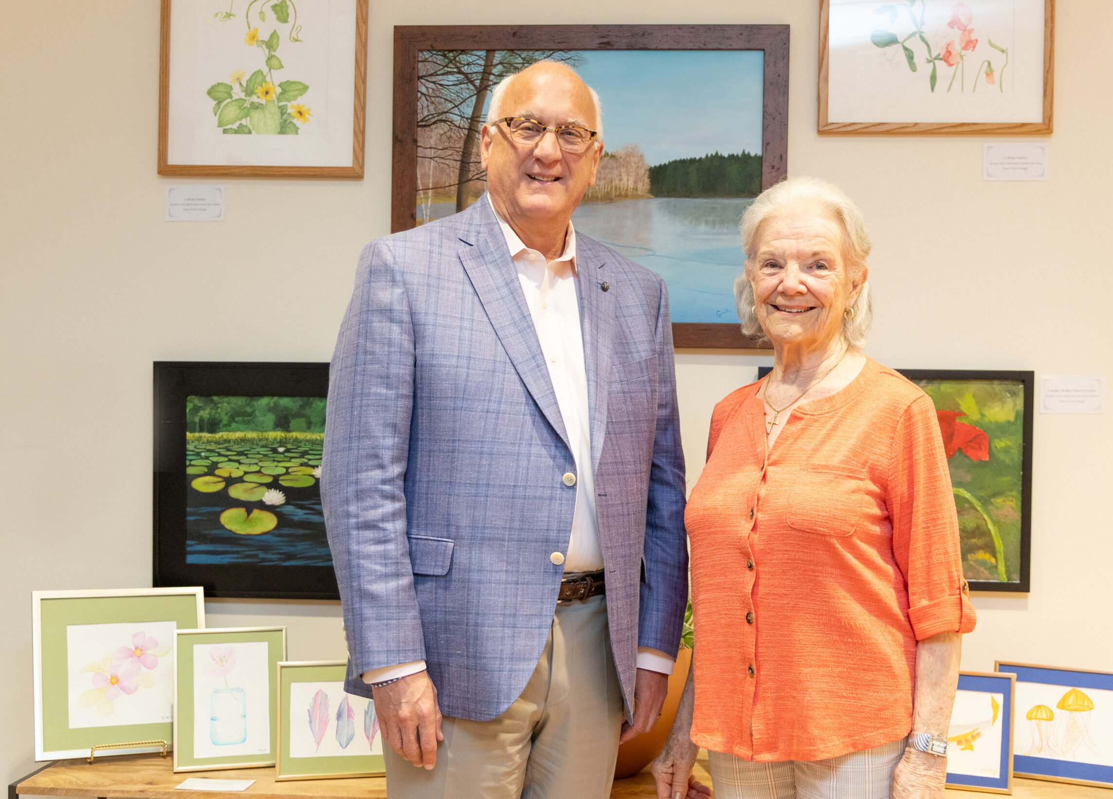 Benchmark CEO Tom Grape and New Pond Village resident artist Celeste Hurley stand in front of an art display at Benchmark Headquarters.