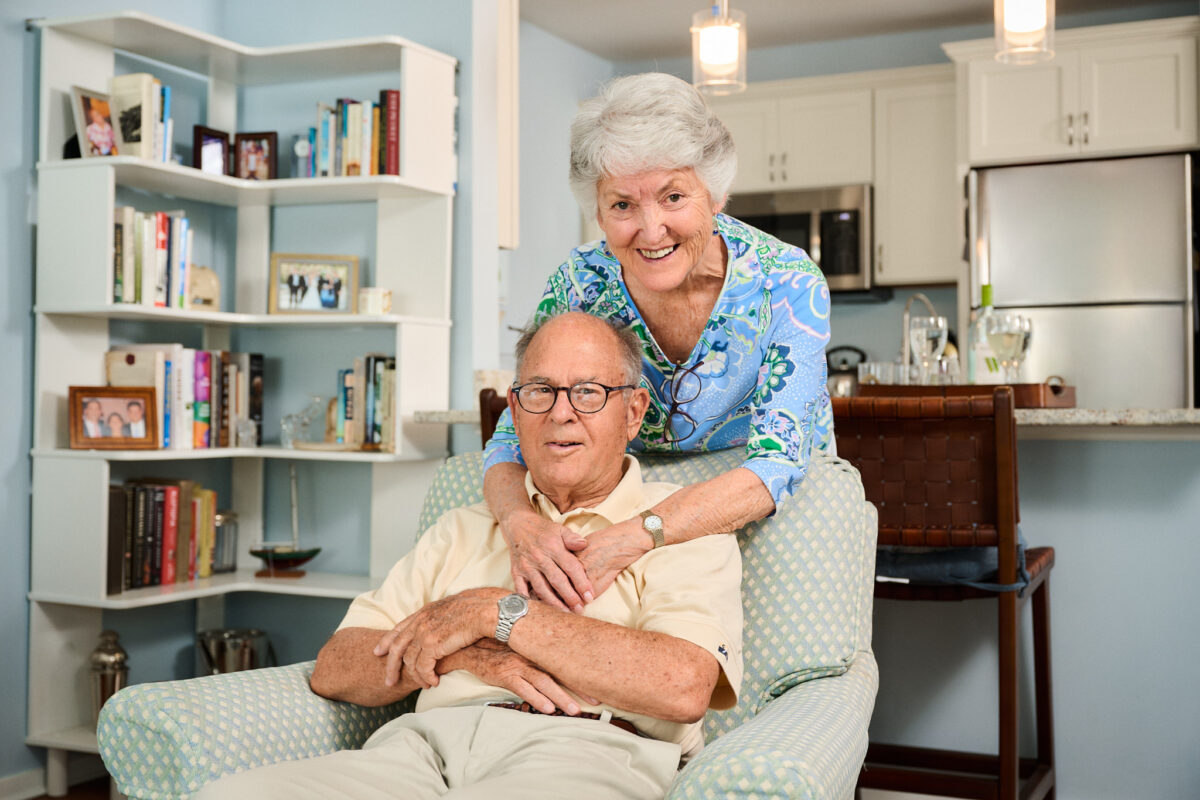 New Pond Village independent living residents Charlie and Stephie Peck smiling together in their brightly decorated apartment home in Walpole, MA.